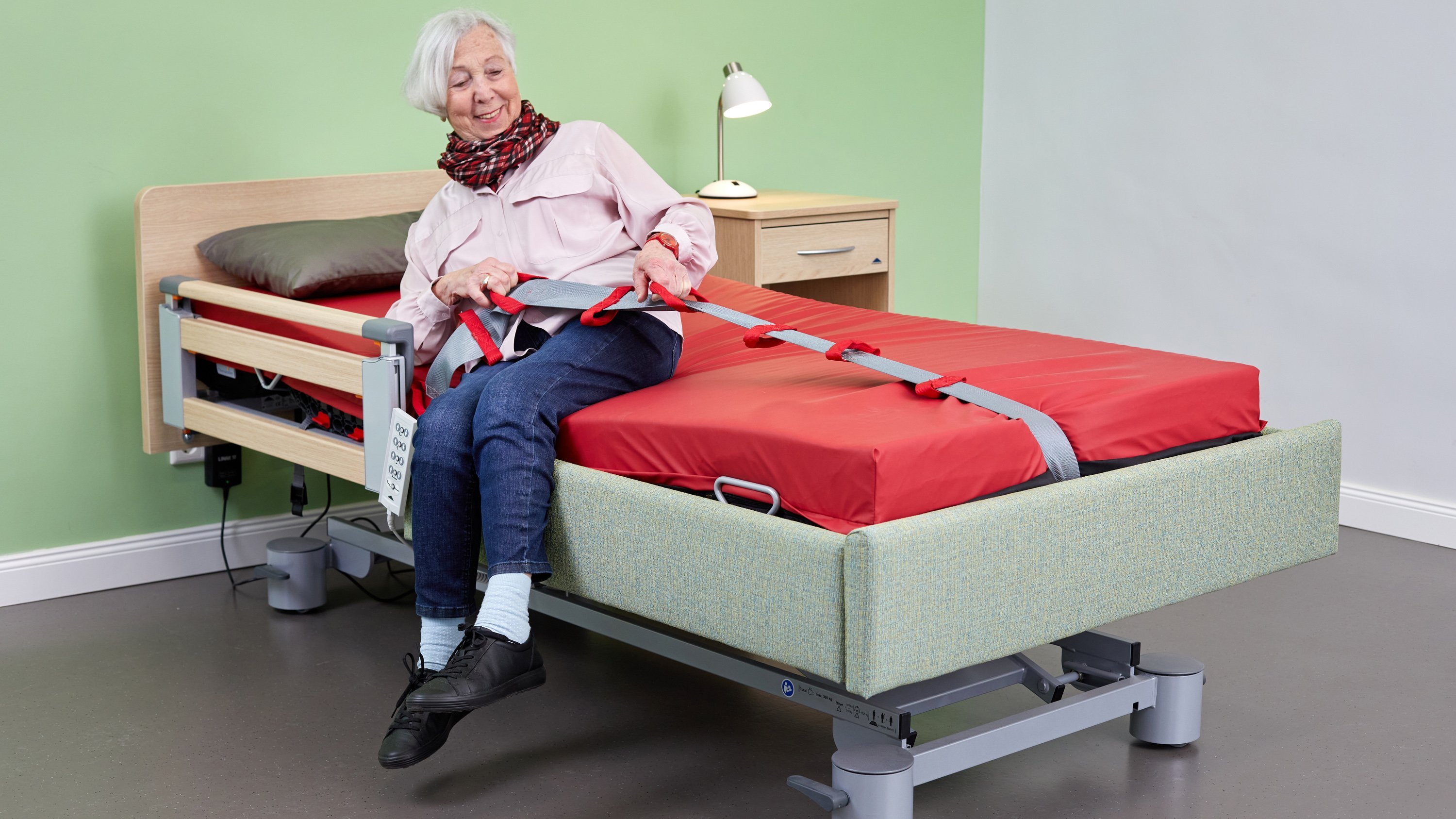 Eine Frau richtet sich in einem Pflegebett mit Hilfe einer textilen Bettleiter auf.