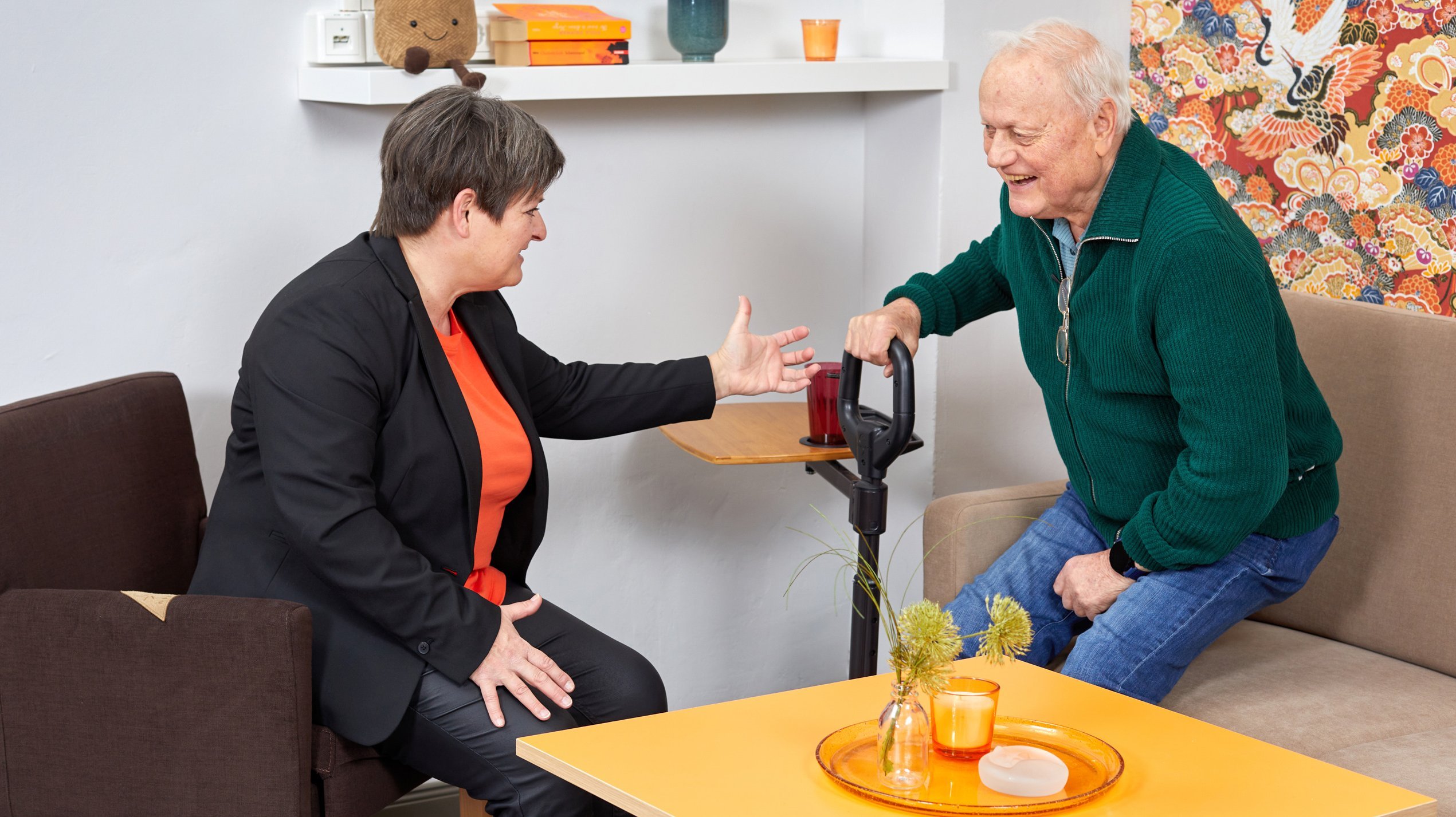 •	Eine Fachberaterin um Gespräch mit einem Ratsuchenden. Ausprobiert wird eine Aufstehhilfe vom Sofa.