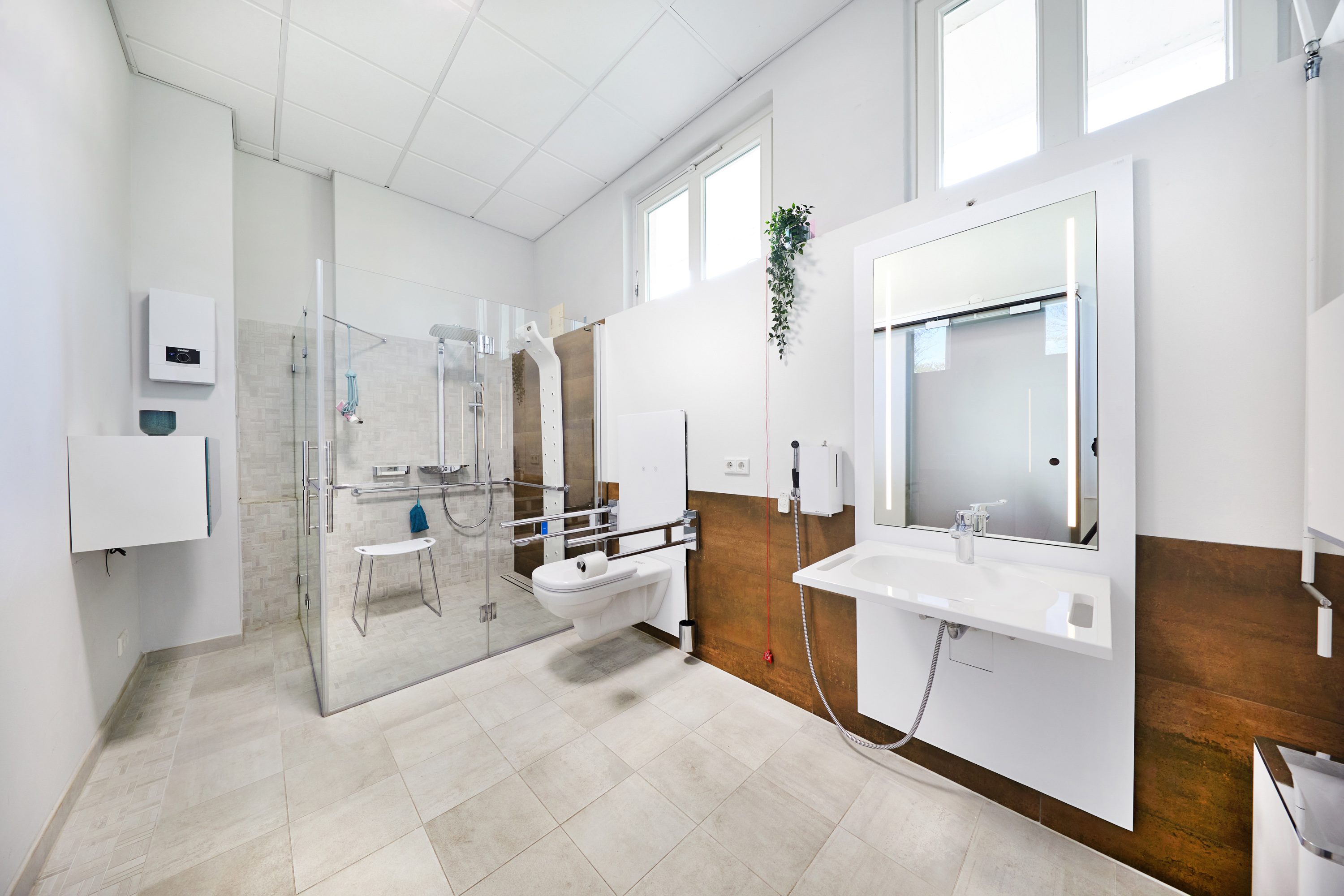Das Bild zeigt ein Ausstellungsbad mit höhenverstellbaren Waschtisch und höhenverstellbaren WC sowie einem rollstuhlgerechten Duschplatz.